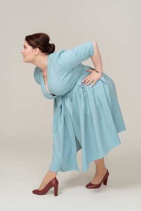 Vista lateral de uma mulher de vestido azul curvando-se
