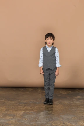 Front view of a boy in suit looking at camera and showing tongue