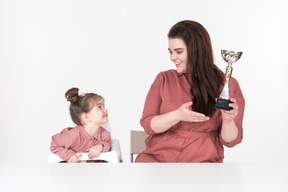 Madre e figlia piccola seduta al tavolo con una coppa del premio