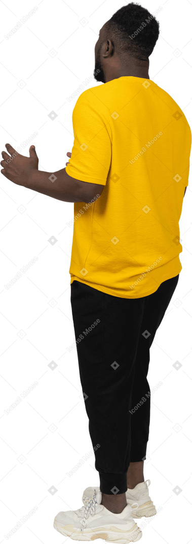 뭔가를 설명하는 노란색 티셔츠를 입고 몸짓을 하는 짙은 피부의 젊은 남자의 3/4 뒷모습