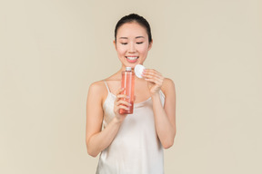 Dreamy young asian girl holding cosmetic bottle and cotton pad