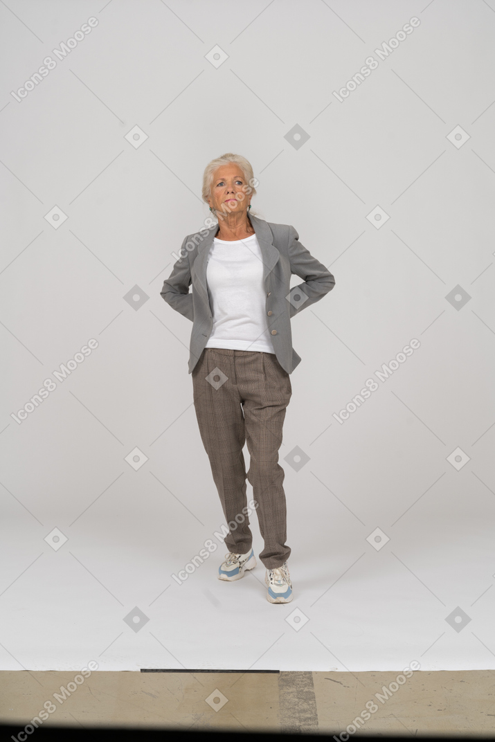Vista frontal de uma senhora idosa de terno em pé com as mãos atrás das costas