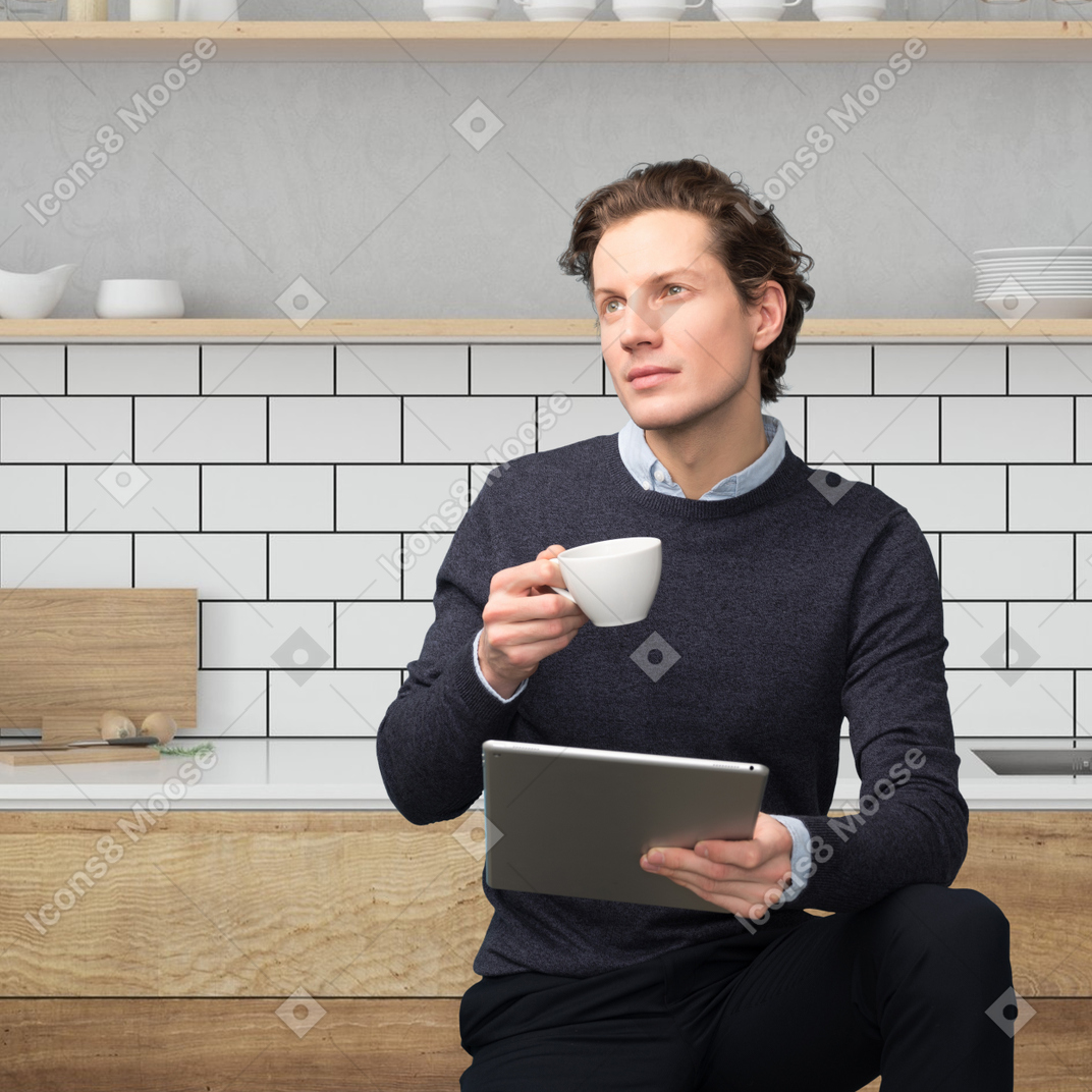 Chico guapo soñador con una taza y una computadora portátil en sus manos