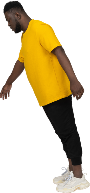 Vista lateral de un joven de piel oscura saltando en camiseta amarilla mirando hacia abajo