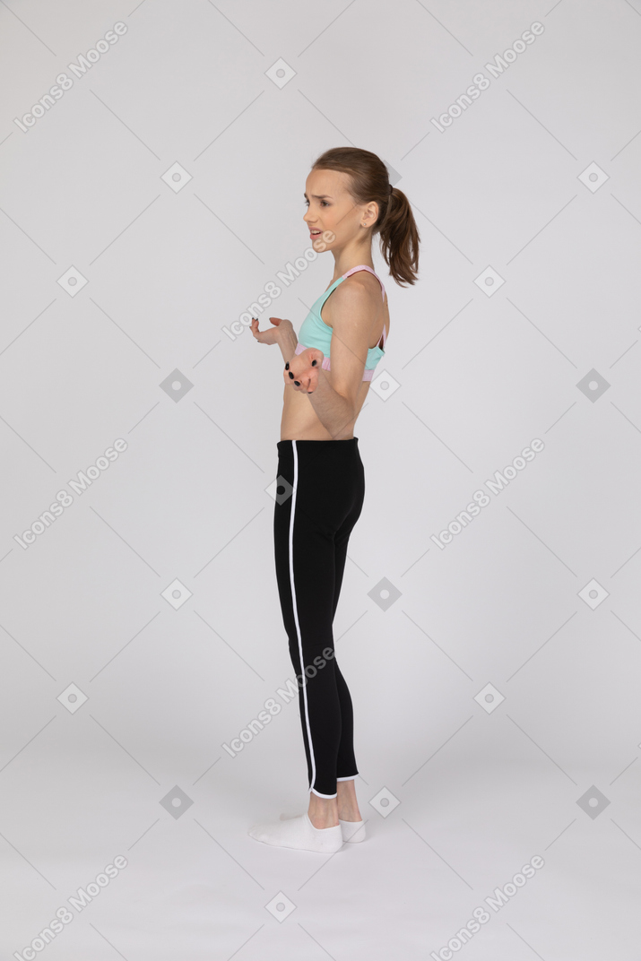 Vista lateral de una adolescente decepcionada con ropa deportiva levantando las manos