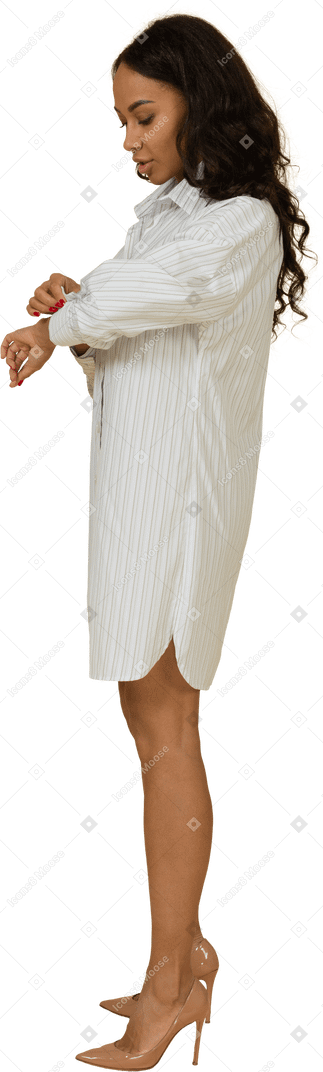 Vue latérale d'une jeune femme à la peau sombre en robe blanche boutonnant sa manche
