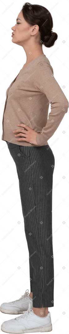 Vista laterale di una giovane donna scontenta in pullover e pantaloni che mette le mani sui fianchi
