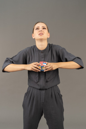 Vista frontal de una mujer joven en un mono tratando de resolver el rompecabezas del cubo de rubik