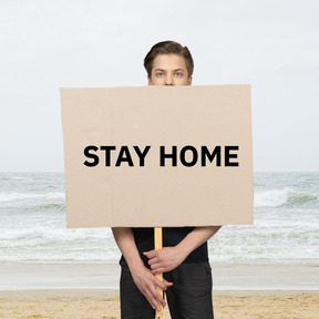 Man standing on the beach with a stay home sign