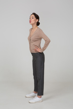 一位年轻的女士，穿着套头衫和裤子pants着嘴，把手放在臀部上的四分之三视图