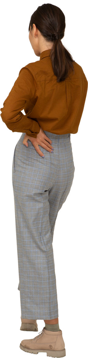Vista posteriore di tre quarti di una giovane donna asiatica in calzoni e camicetta che mette la mano sull'anca