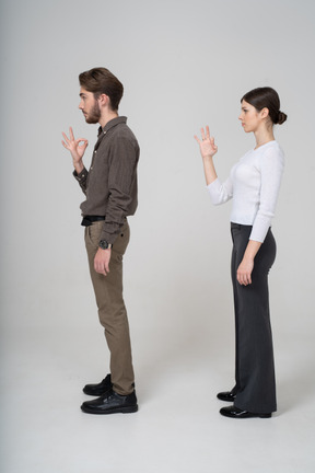 Side view of a young couple in office clothing showing ok sign