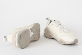 A three-quarter shot of a pair of white and beige sneakers, with one of them lying on its side