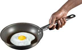 Человеческая рука держит жареное яйцо на сковороде