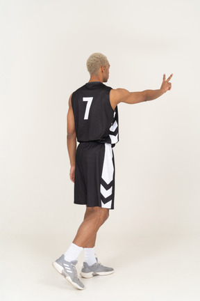 Vista posterior de tres cuartos de un joven jugador de baloncesto masculino que muestra el signo de la paz