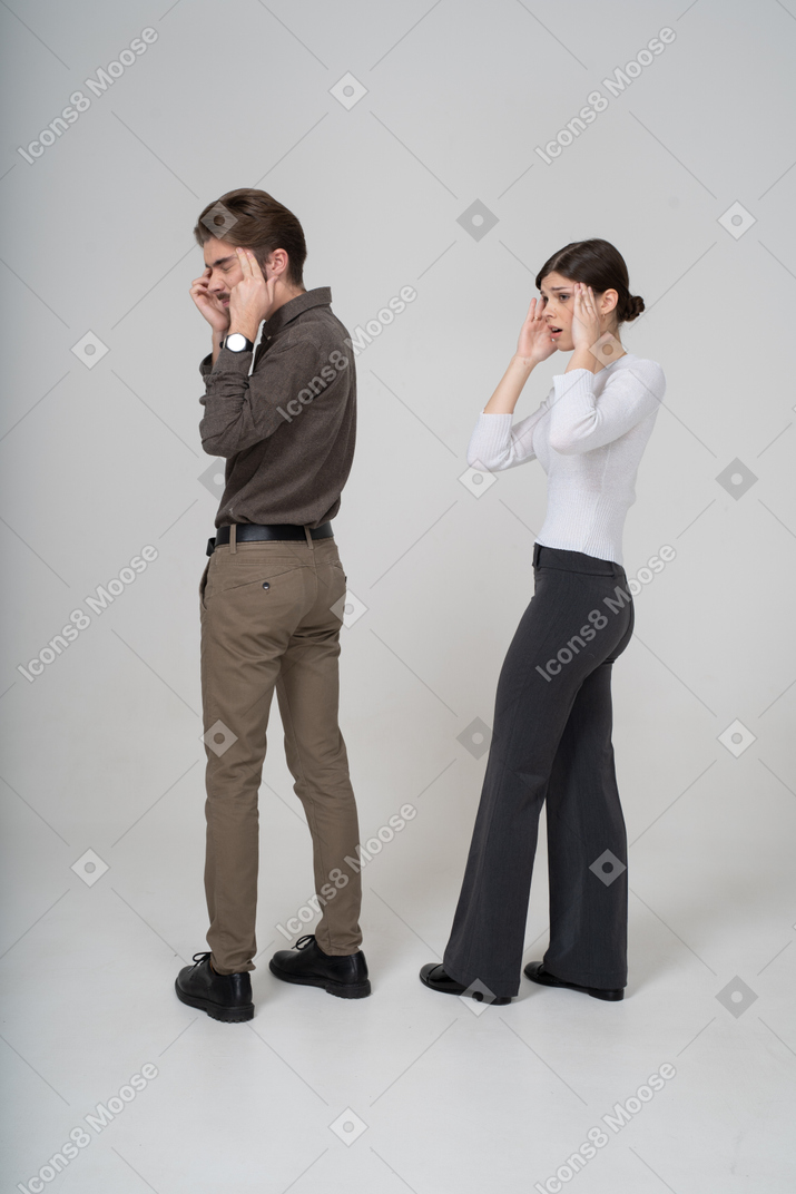 Vista traseira de três quartos de um jovem casal chocado com roupas de escritório tocando a cabeça