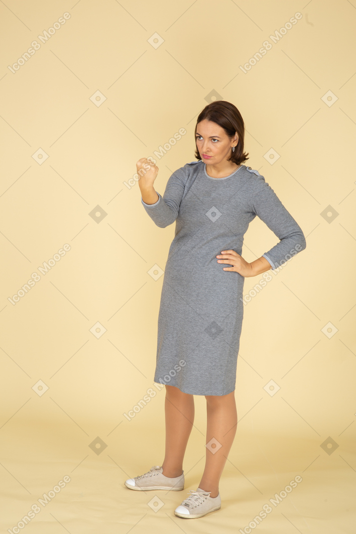Front view of a woman in grey dress threatening someone with fist