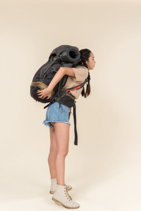 Joven excursionista mujer llevando mochila pesada y de pie de nuevo a la cámara