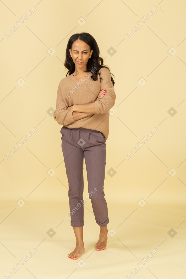 Vista frontal de un guiño joven mujer de piel oscura cruzando los brazos