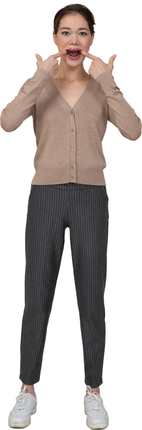 Front view of a young lady in pullover and pants touching her mouth