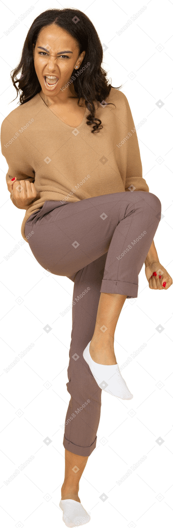 Vista frontal de una fresca mujer joven de piel oscura levantando la pierna y apretando el puño