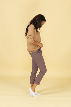 Vista lateral de uma jovem mulher de pele escura fechando o zíper das calças