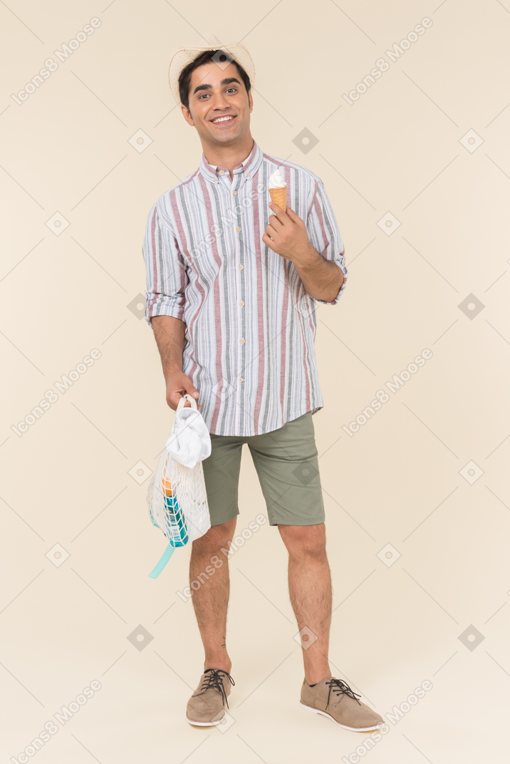 Smiling young caucasian guy holding avoska and eating ice cream