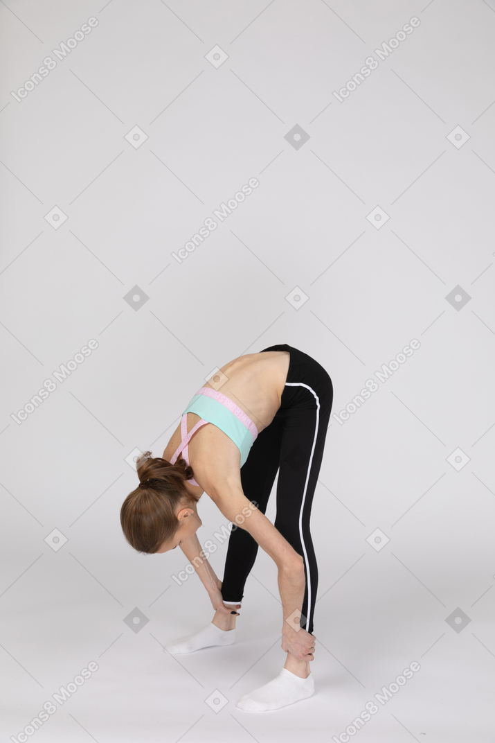 Вид сбоку девушки-подростка в спортивной одежде, сидящей на корточках и кладущей руки на бедра