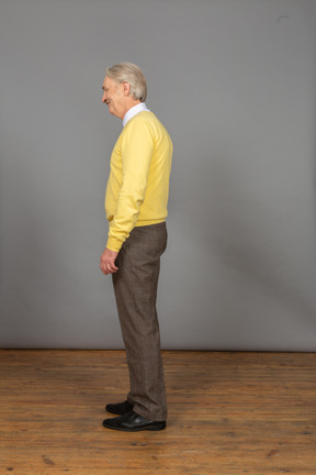 Vista laterale di un uomo anziano sorpreso in pullover giallo chinandosi e guardando da parte