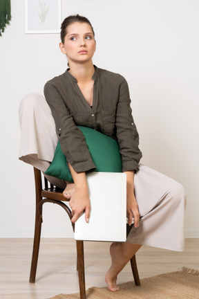 Front view of a confused young woman sitting on a chair and holding her laptop