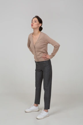 Three-quarter view of a young lady in pullover and pants sending an air kiss and putting hands on hips