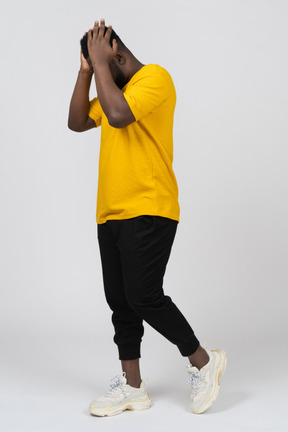 Side view of a walking young dark-skinned man in yellow t-shirt touching head