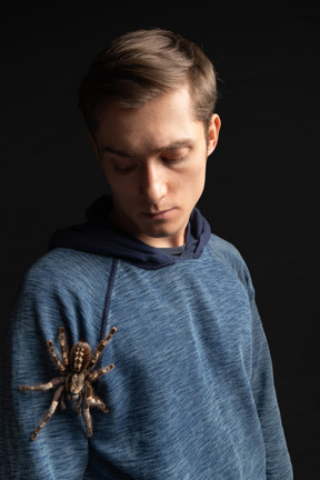 Young man looking at big tarantula creeping on his shoulder