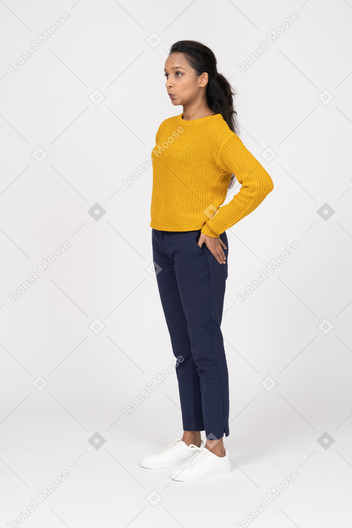 Side view of a girl in casual clothes standing with hand on hip and making faces