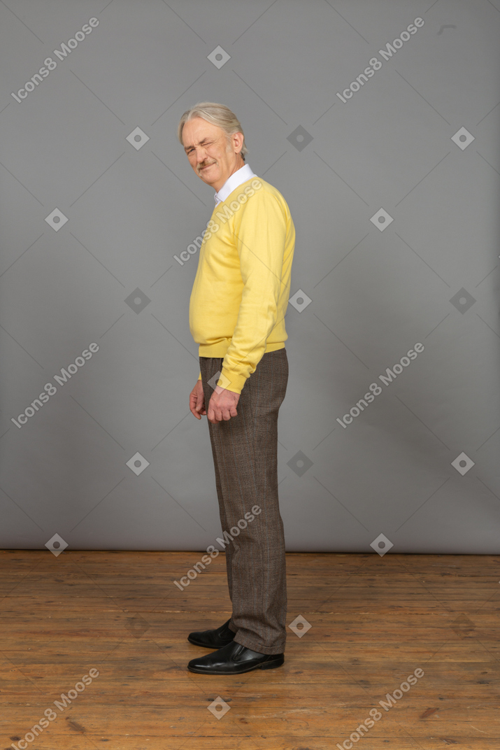 노란색 스웨터에 노련한 불쾌한 남자의 측면보기 눈을 좁히고 카메라를보고