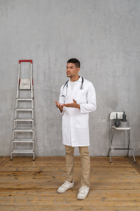 Vue de trois quarts d'un jeune médecin debout dans une pièce avec échelle et chaise expliquant quelque chose