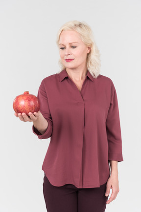 A nice-looking middle-aged blonde woman in a burgundy shirt and a pomegranate in her hand