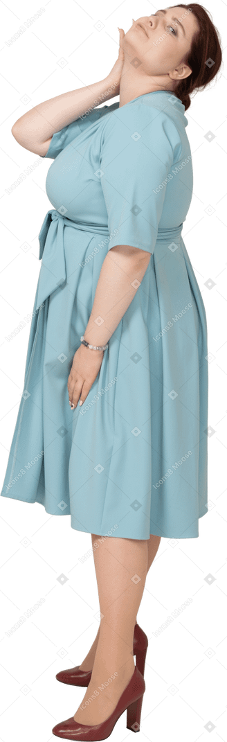 Vue latérale d'une femme en robe bleue posant avec la main sur le cou