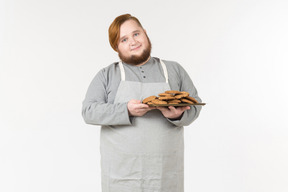 Um padeiro gordo sorridente segurando um prato de biscoitos