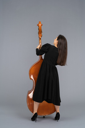 Vue arrière d'une jeune femme musicienne en robe noire tenant sa contrebasse