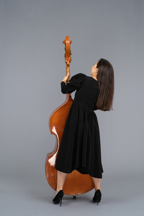 Vista de trás de uma jovem musicista vestida de preto segurando seu contrabaixo