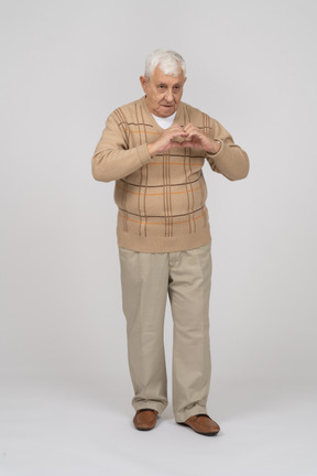 Vista frontal de un anciano con ropa informal haciendo corazón con los dedos