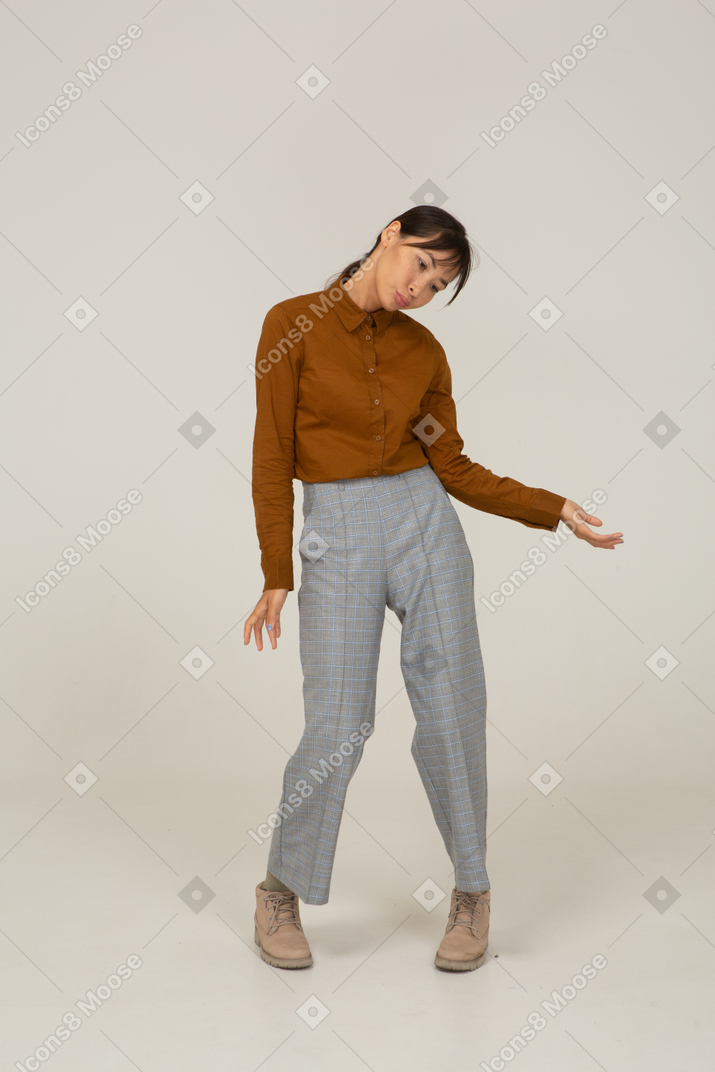 Vista lateral de uma jovem mulher asiática de calça e blusa, inclinando a cabeça e estendendo a mão