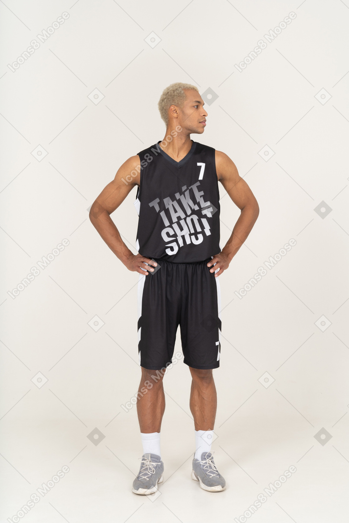 Vista frontal de un joven jugador de baloncesto masculino poniendo las manos en las caderas y mirando a un lado