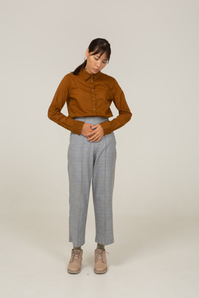 Vista frontale di una giovane donna asiatica in calzoni e camicetta che tocca lo stomaco