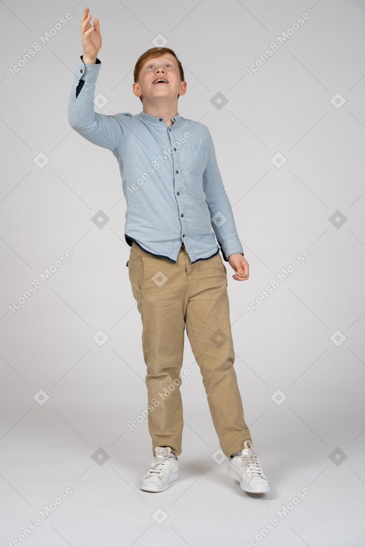 Vista frontal do menino bonito apontando para cima com uma mão