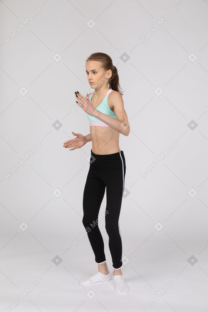 Vista di tre quarti di una ragazza adolescente in abbigliamento sportivo in piedi come un robot