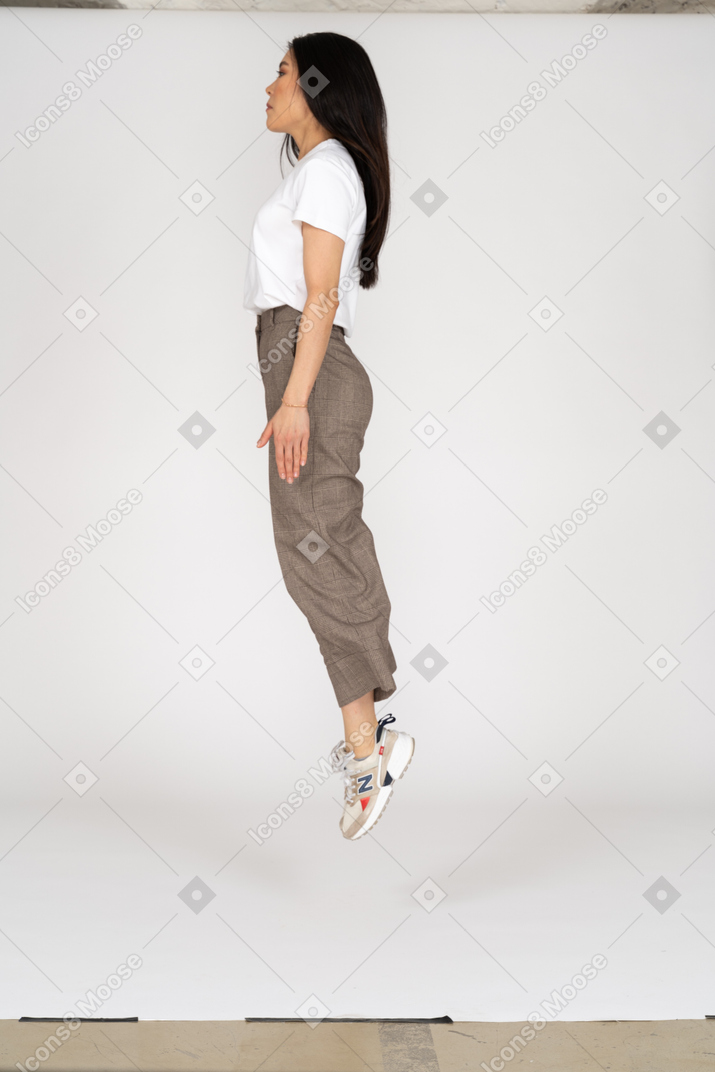 Vista lateral de uma jovem saltitante de calça e camiseta