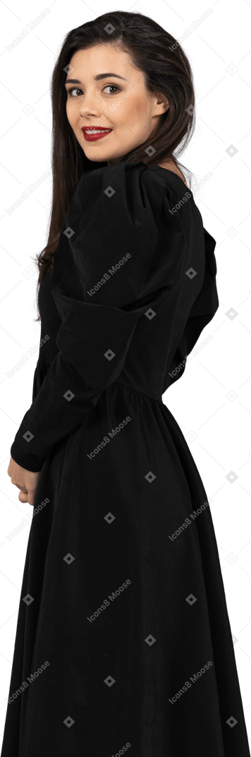 Vista lateral de uma jovem em um vestido preto parada e olhando para a câmera