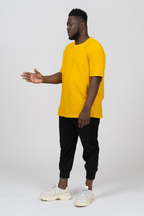 Vista di tre quarti di un giovane uomo dalla pelle scura in maglietta gialla che allunga il braccio